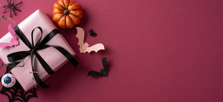 Festive Halloween-themed arrangement featuring a pink gift box with decorations such as bats, a pumpkin, and a spider on a vivid background enhancing the Halloween holiday vibeの写真素材
