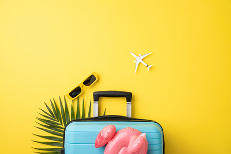Bright travel flat lay with a suitcase, palm leaf, sunglasses, and a toy flamingo, airplane on yellowの写真素材