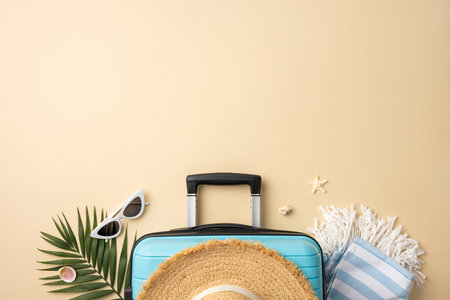 Top view of summer vacation items including a suitcase, straw hat, sunglasses, palm leaf, and striped towel, arranged on a beige background, symbolizing leisure, relaxation, and tropical getawaysの写真素材