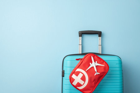 A symmetrical image of a blue suitcase is complemented by a red travel emergency kit. Travel essentials are organized on a minimal blue backgroundの写真素材