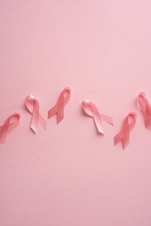Many light pink ribbons symbolizing breast cancer awareness on a soft vertical pink surface