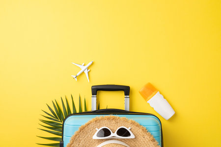 Flat lay composition featuring travel essentials including a suitcase, sunglasses, and tropical accents on a vibrant yellow backdrop, evoking a summer vacation conceptの写真素材