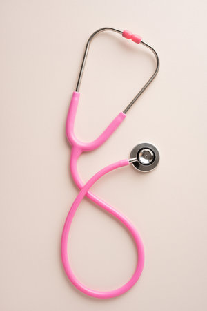 Pink vertical stethoscope placed on a beige background, representing health, care, and awarenessの写真素材