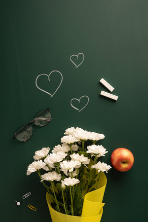 White flowers and an apple placed on a vertical chalkboard with hearts and chalk symbols. Symbolic of teacher appreciationの写真素材