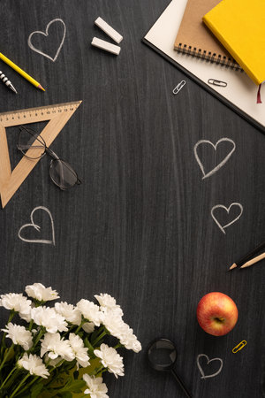 Chalk hearts, stationery supplies, flowers, and an apple arranged on a vertical blackboard inspires a teachers day atmosphereの写真素材