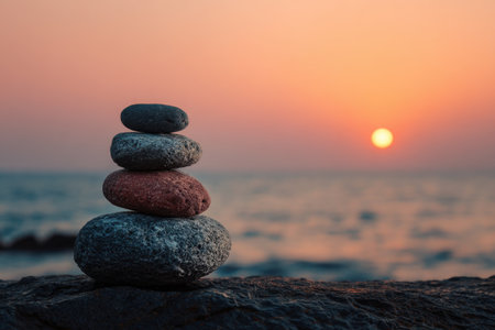 Stacked stones at sunrise over calm ocean waves and warm skyの素材