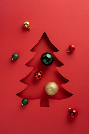 A vertical festive red backdrop featuring a cutout Christmas tree decorated with colorful ornamentsの写真素材
