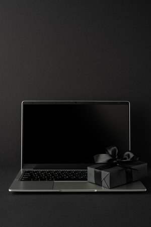 An open vertical laptop and a wrapped gift box with a bow displayed on a dark surfaceの写真素材