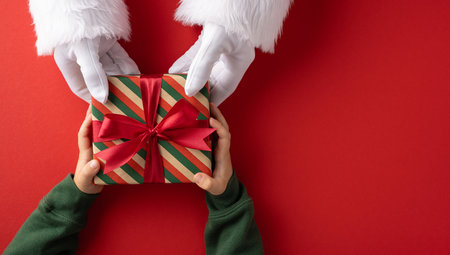 Santa handing a red ribbon gift to a child during Christmas seasonの写真素材