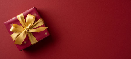 A festive red gift box tied with a gold ribbon sits on a rich red backdrop, capturing holiday warmth, celebration, and the spirit of Christmas and New Yearの写真素材