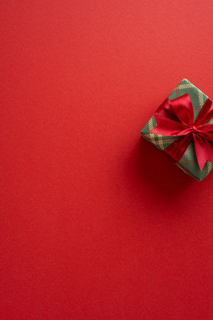 A vertical plaid green gift box with a bright red ribbon sits on a bold red background, creating a festive mood, warmth, and holiday cheer for Christmas and New Year celebrationの写真素材