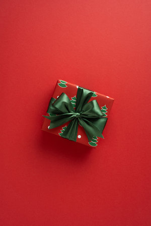 A festive vertical gift box with a lush green ribbon sits against a bold red backdrop, symbolizing Christmas joy and New Year cheer. Ideal for holiday greeting, celebration and seasonal decor promotesの写真素材