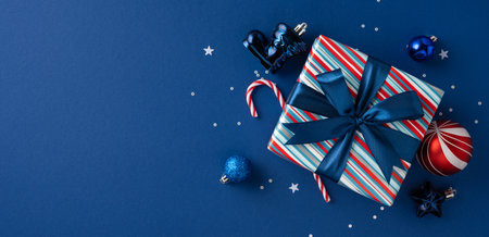 A blue banner background highlights a striped gift box tied with a dark ribbon, surrounded by candy canes and ornaments to evoke Christmas and New Year celebrations and gift givingの写真素材