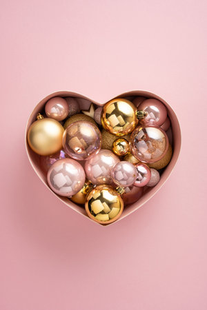 Pink vertical background with a heart shaped box overflowing with glass Christmas ornaments, perfect for festive decor, holiday season celebrations, and New Year greetingsの写真素材