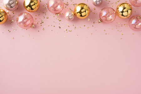 A soft pink backdrop showcases gold and pink ornaments with metallic confetti, creating a chic holiday scene ideal for seasonal promotions, greeting cards, and festive campaignsの写真素材