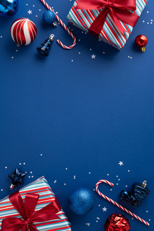 Bright vertical Christmas and New Year scene with striped gifts, baubles, candy canes, and confetti on a blue backdrop, conveying festive joy, gifting, and seasonal cheerの写真素材