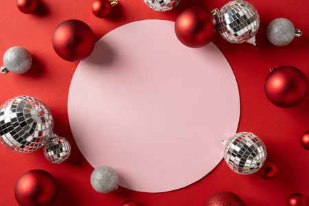 Vibrant holiday scene with red and silver ornaments framing a soft pink circle, evoking festive mood and greeting for Christmas and New Year events and promotionsの写真素材
