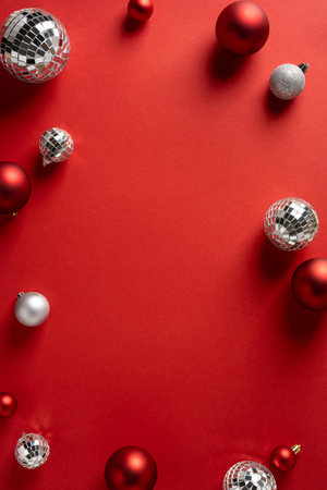 Vertical scene with a red backdrop and shiny ornaments, disco balls, and silver baubles creating a festive mood for Christmas and New Year greetingの写真素材