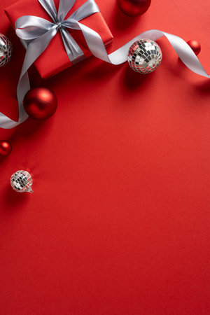 Vertical holiday scene featuring a red gift box with silver ribbon and shiny ornaments, conveying festive spirit and Christmas NewYear celebrationの写真素材