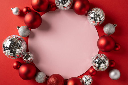 Red and silver ornaments frame a pink circular backdrop, creating a festive scene for Christmas and New Year greetings, holiday decor and seasonal celebrationの写真素材