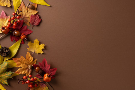 Autumn themed composition with a left border of colorful leaf shapes, berries and a pinecone on a...