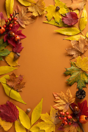 Vertical autumn frame of colorful leaves and berries on an orange backdrop, showcasing seasonal...