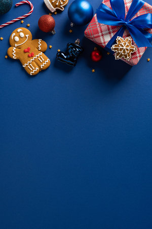 A festive vertical scene featuring a wrapped gift, gingerbread cookie, candy canes, and decorative ornaments set on a deep blue backdrop, ideal for Christmas and New Year greetings and holiday decorの写真素材