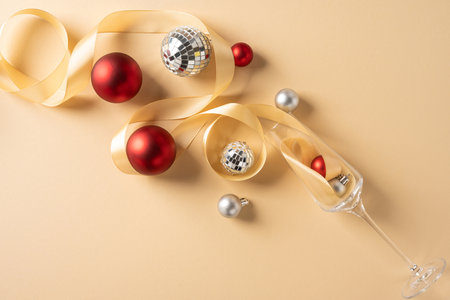 Festive scene featuring champagne flute, ribbons, red and silver ornaments on a warm beige backdrop. Elegant decor conveys holiday celebration, glamour, seasonal merryment for Christmas and New Yearの写真素材