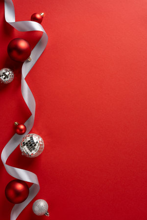 Vertical scene on red backdrop with silver ribbon and festive ornaments, ideal for Christmas and New Year greeting campaigns, festive promotion, celebration mood, and seasonal designの写真素材