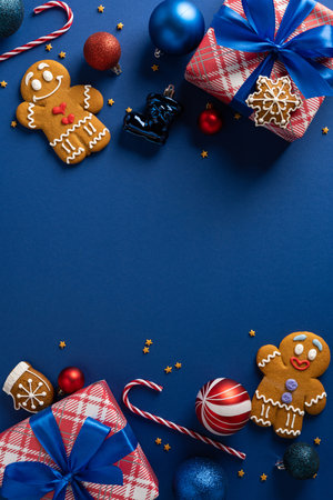 A vertical bright holiday scene featuring wrapped gifts, gingerbread cookies, candy canes, ornaments and glittering accents on a blue backgroundの写真素材