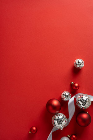 Vertical festive arrangement on a bold red backdrop featuring silver disco balls, red ornaments, and white ribbon, perfect for Christmas and New Year greeting concepts and holiday celebrationの写真素材