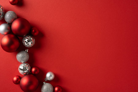Vibrant holiday scene with red and silver Christmas ornaments arranged along a curved edge, creating a festive focal point on a bold red backdropの写真素材