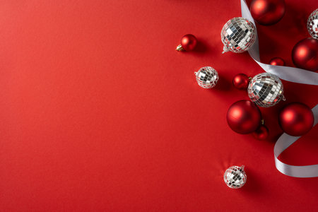 Vibrant red background with silver disco balls, red baubles, and white ribbon creates a festive mood perfect for Christmas and New Year greetings and seasonal gift themesの写真素材