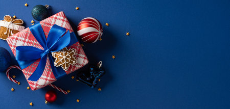A red plaid gift box tied with a vivid blue ribbon sits on a dark blue background, surrounded by ornaments, stars, and candy canes, evoking Christmas anticipation and New Year festivityの写真素材