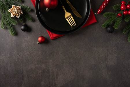 A stylish holiday scene featuring a dark plate, gold cutlery, red napkin, and festive greens with ornaments, capturing the mood of Christmas and New Year celebrationの写真素材
