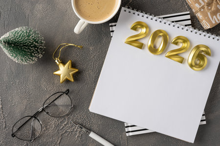 Festive desk scene featuring a white calendar marked 2026 in gold, a small Christmas tree, golden...