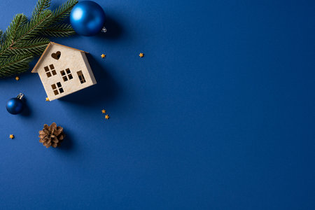A festive blue background hosts a tiny wooden house ornament, pine branch, blue baubles, and a pine cone, evoking a simple cozy seasonal vibe tied to Christmas and New Year celebrationsの写真素材