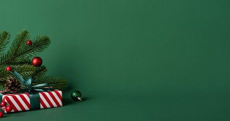 A green backdrop frames a festive Christmas gift with a pine sprig, red baubles, and a striped present, conveying holiday warmth, seasonal joy, and New Year celebration vibesの写真素材