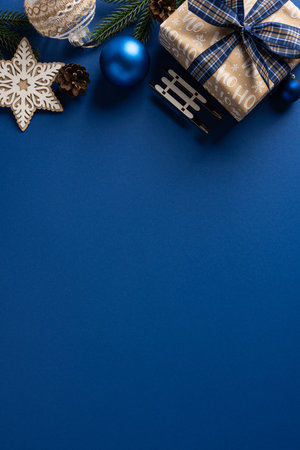 Blue vertical holiday backdrop with a wrapped gift, wooden snowflake, pine cones, and a blue ornament create a festive Christmas and New Year mood perfect for greetings, decor, and celebration themesの写真素材
