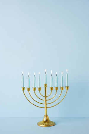 Golden vertical Hanukkah menorah with blue candles glows on a pale blue backdrop. Symbolic festival of lights, tradition, and celebrationの写真素材