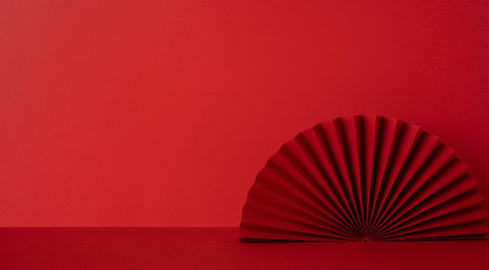 Side view of a red studio scene with a folded paper fan on a flat surface, symbolic of Chinese New Year greeting, warm mood, festive color, celebration, tradition, hope, luck, prosperity, cultureの写真素材