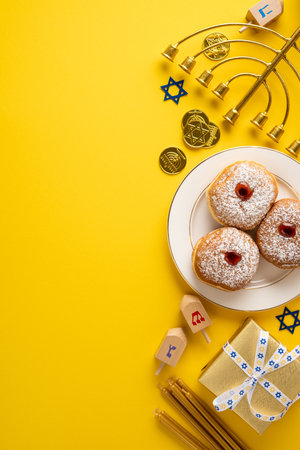 Vibrant vertical Hanukkah display featuring pastries, dreidel, menorah, coins, and a gift box on a sunny yellow backdrop. Warmth, tradition, and festive symbols convey holiday celebration and cheerの写真素材