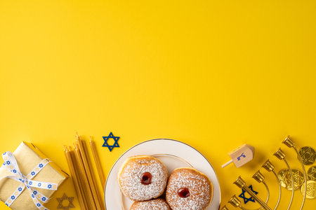 A festive Hanukkah scene features sufganiyah donuts, a lit menorah, a spinning dreidel, and a gift on a sunny yellow backdrop. Warm, celebratory mood suitable for greeting cards and seasonal campaignsの写真素材