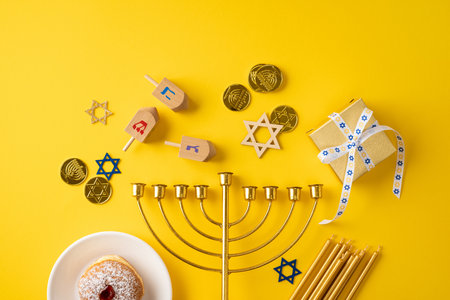 Bright Hanukkah scene features a central menorah, dreidel, coins, a gift box, and Star of David motifs on a vibrant yellow backdropの写真素材