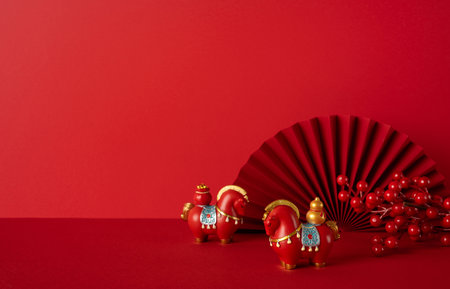 Side view of a red Chinese New Year scene featuring ornamental figures, a large fan, and bright berries, conveying festive greeting and wishes of luck and prosperityの写真素材