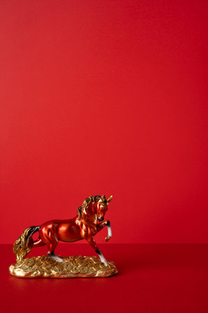 Side vertical view of a gold horse statue on a decorative base against a bold red backdrop, symbolizing luck, prosperity, and a Chinese New Year greeting traditionの写真素材
