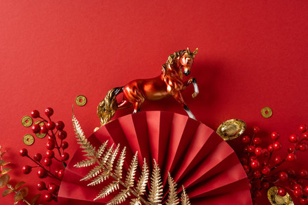 Vibrant red backdrop featuring a decorative horse statue atop a stylized fan, gold coins, and red berries to evoke prosperity, luck, and festive Chinese New Year greetingsの写真素材