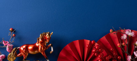 A festive scene with a golden horse statue, red fan and blossoms set against a deep blue backdrop, conveying luck, prosperity and traditional celebration.の写真素材
