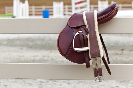 A dark english saddle sits on a fence with jumps in the backgroundの写真素材