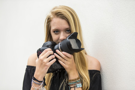 A teenage blonde model posing outdoors with a DSLR cameraの写真素材